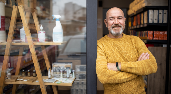 Image d’un homme souriant en pull orange avec les bras croisés sur le pas d’une porte